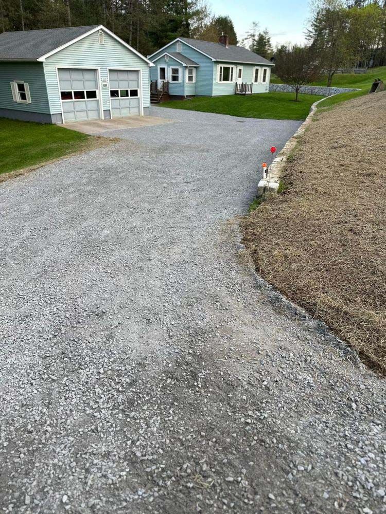A gravel driveway leading to a house and a garage.