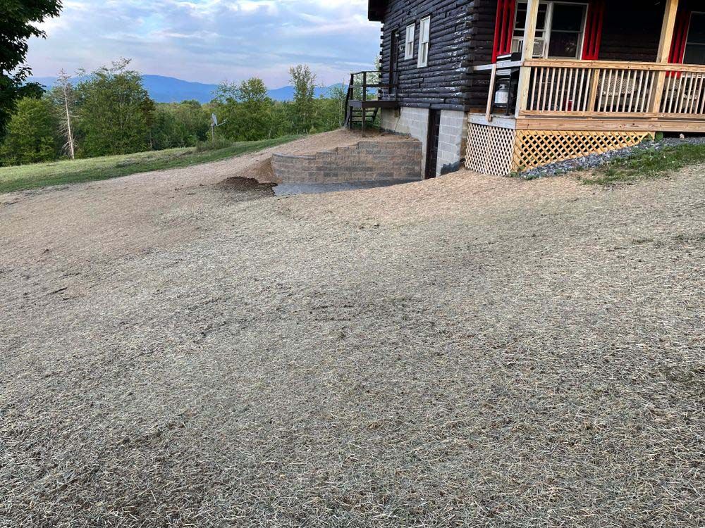 A house with a porch and a gravel driveway in front of it.