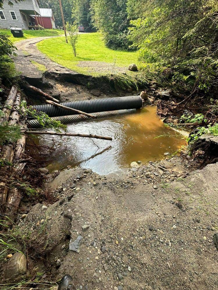 A stream of water is coming out of a pipe in the middle of a dirt road.