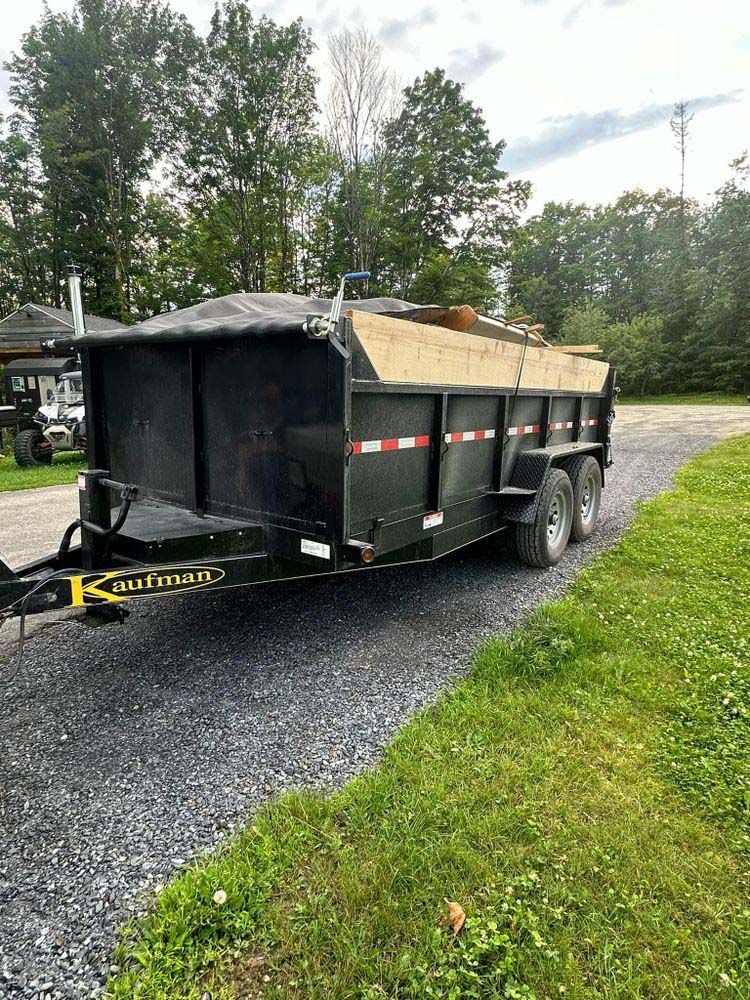 A dump trailer is parked on the side of a gravel road.
