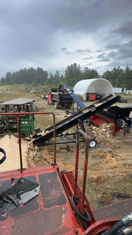 A red truck is parked in a field next to a conveyor belt.