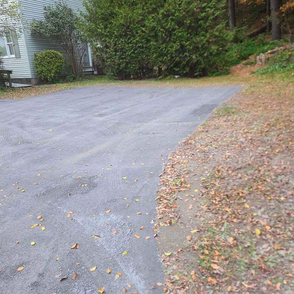 A driveway with leaves on the ground and a house in the background