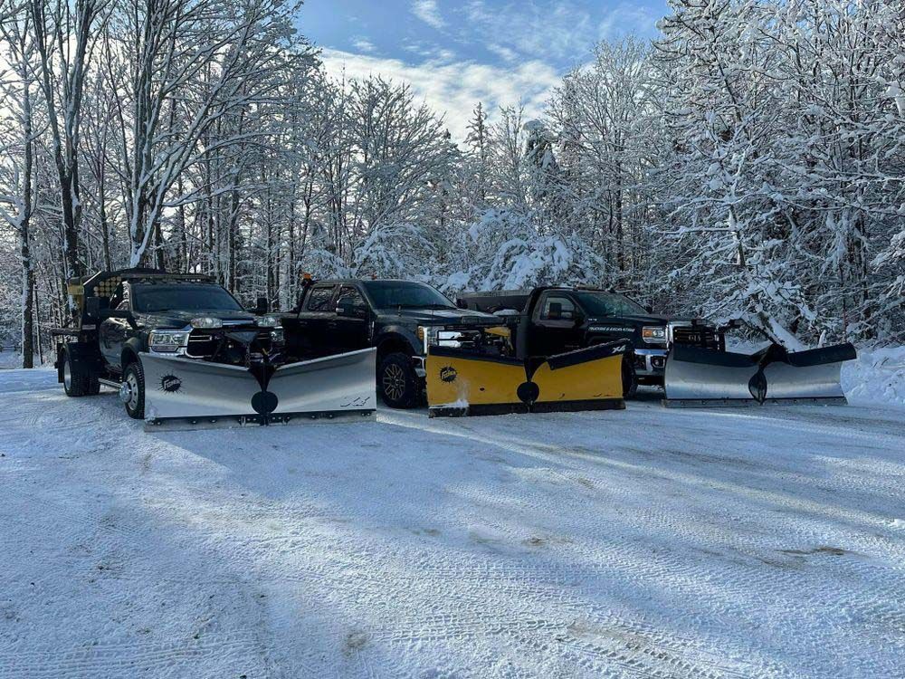 A group of snow plows are parked in a snowy parking lot.