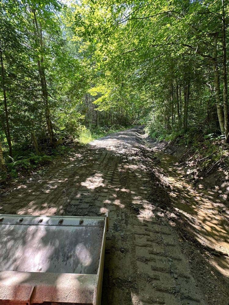A tractor is driving down a dirt road in the woods.