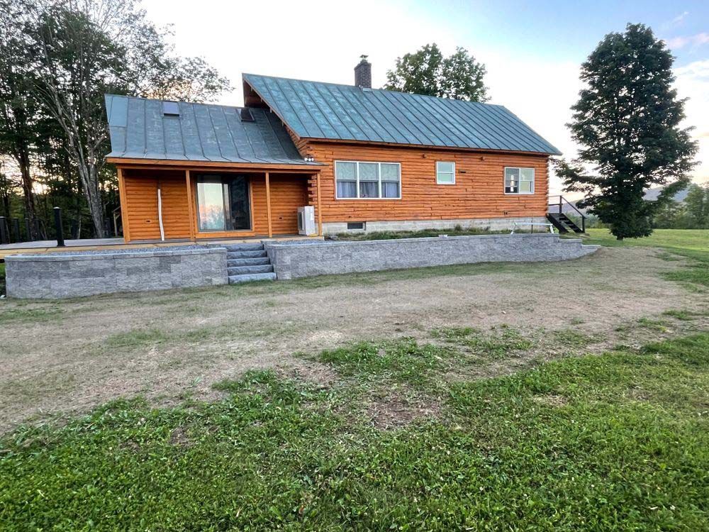 A log cabin with a metal roof is sitting in the middle of a grassy field.