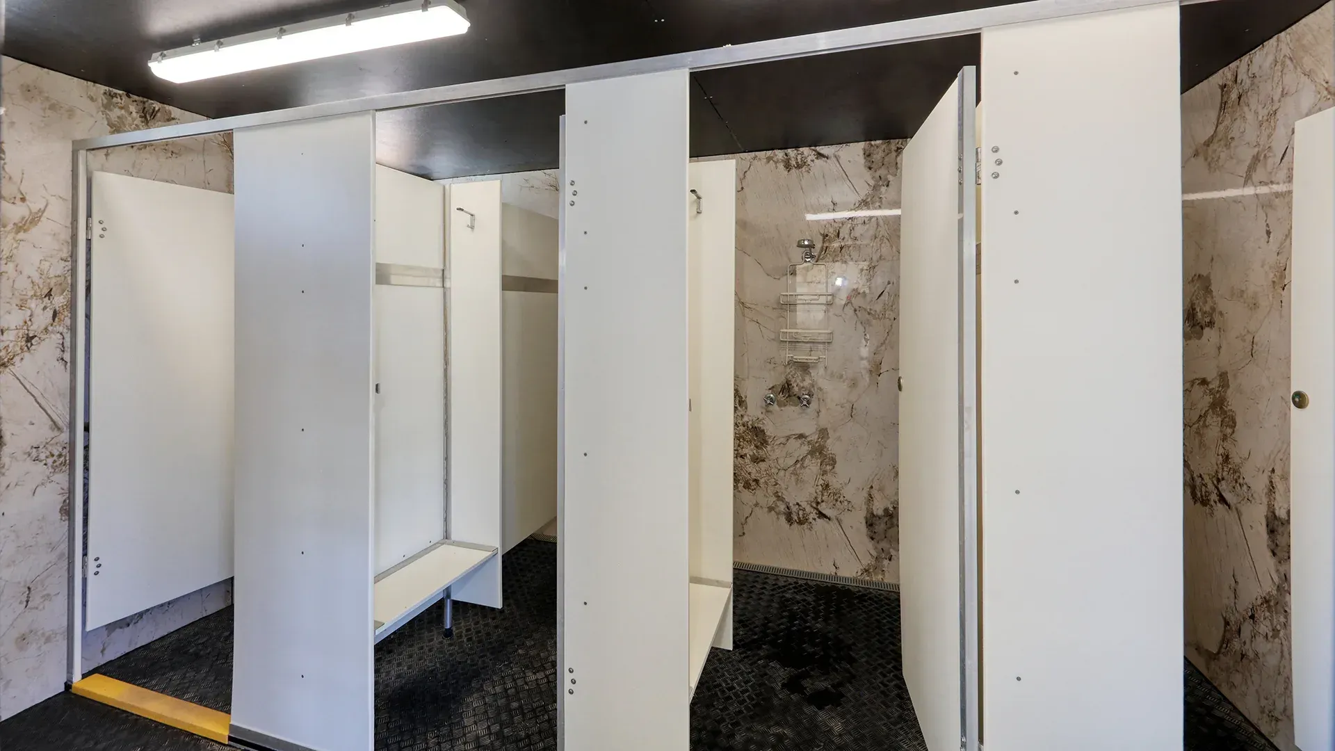 Row of white restroom stalls with open doors in a worn, dimly lit interior.