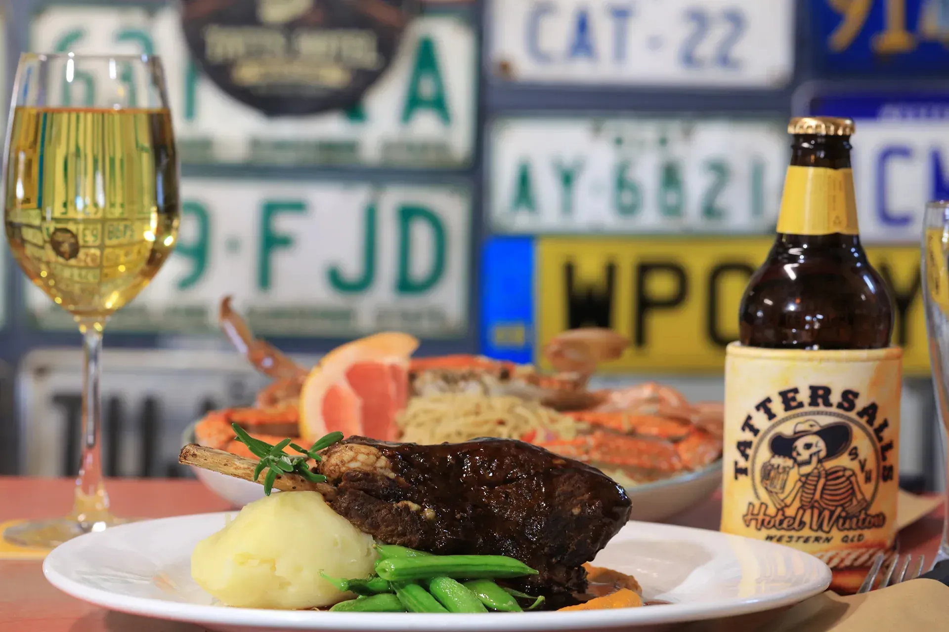 Plated steak dinner with vegetables beside a glass of white wine and a beer bottle on a table