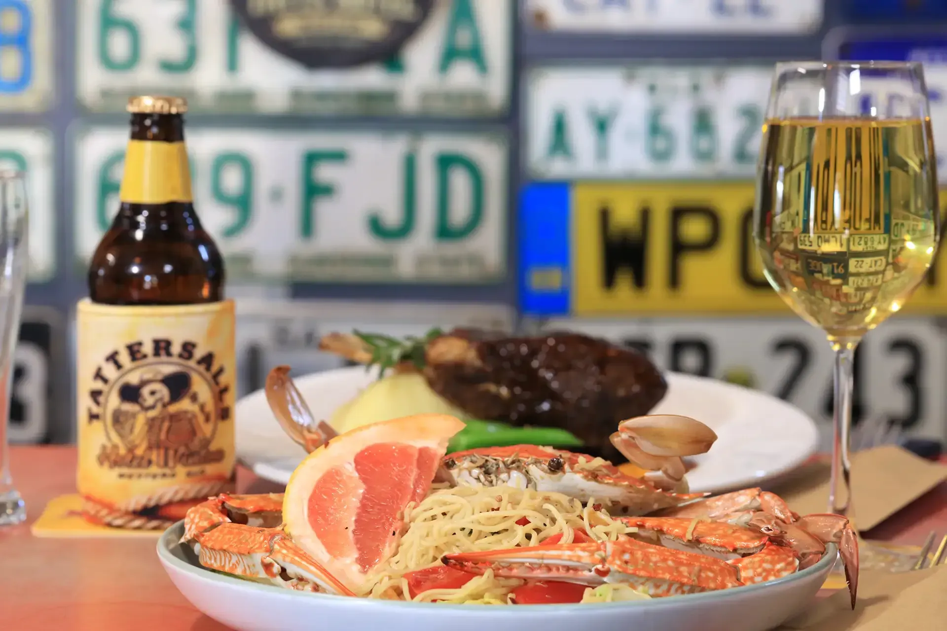 Seafood platter with beer and a wine glass on a table, against a background of license plates.