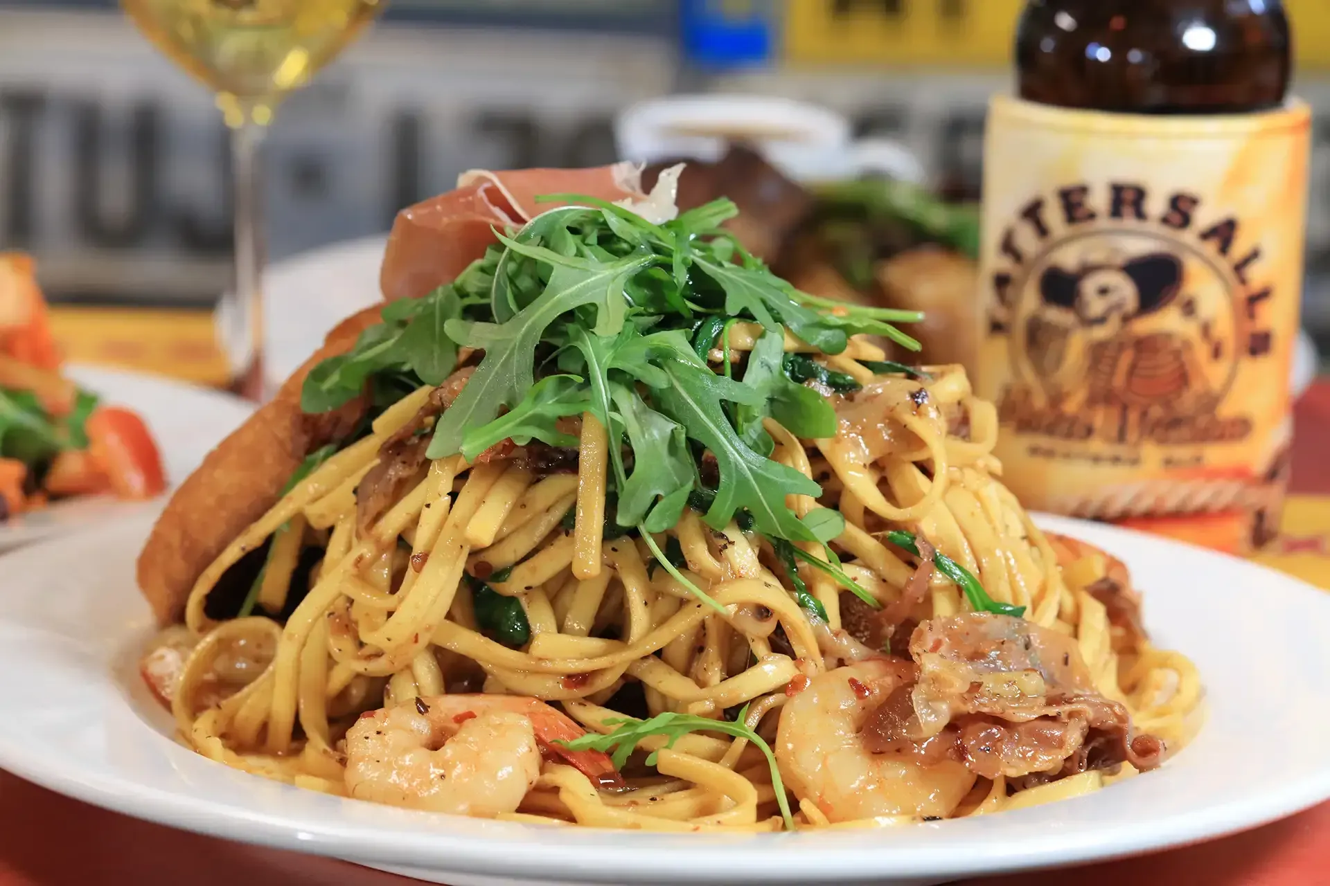 Plate of pasta with greens and shrimp, with a Bierstube beer bottle in the background