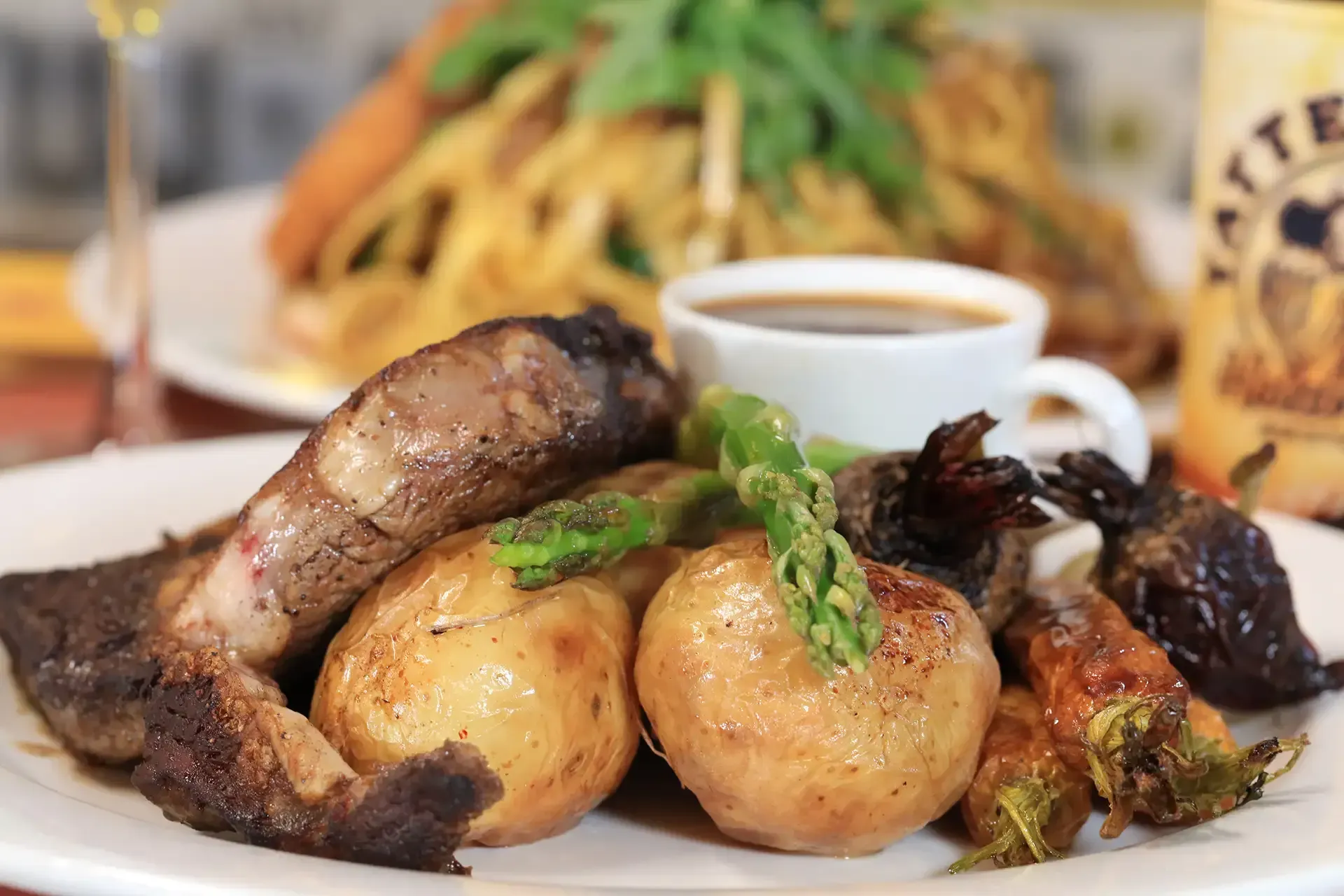 Roasted potatoes and sausages on a plate with asparagus and sauce at a restaurant table