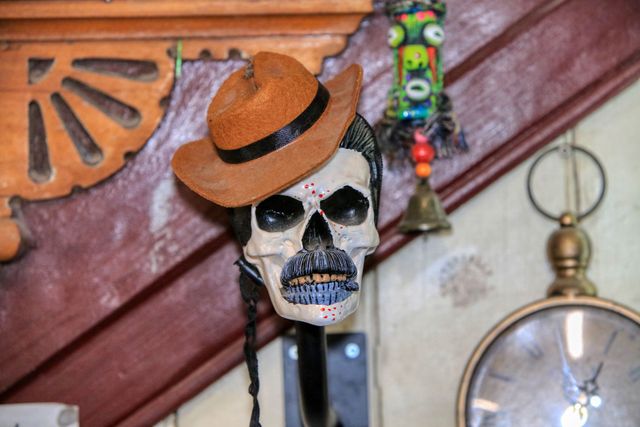 Skeleton skull wearing a brown hat, hanging indoors beside a clock and decorative carving.
