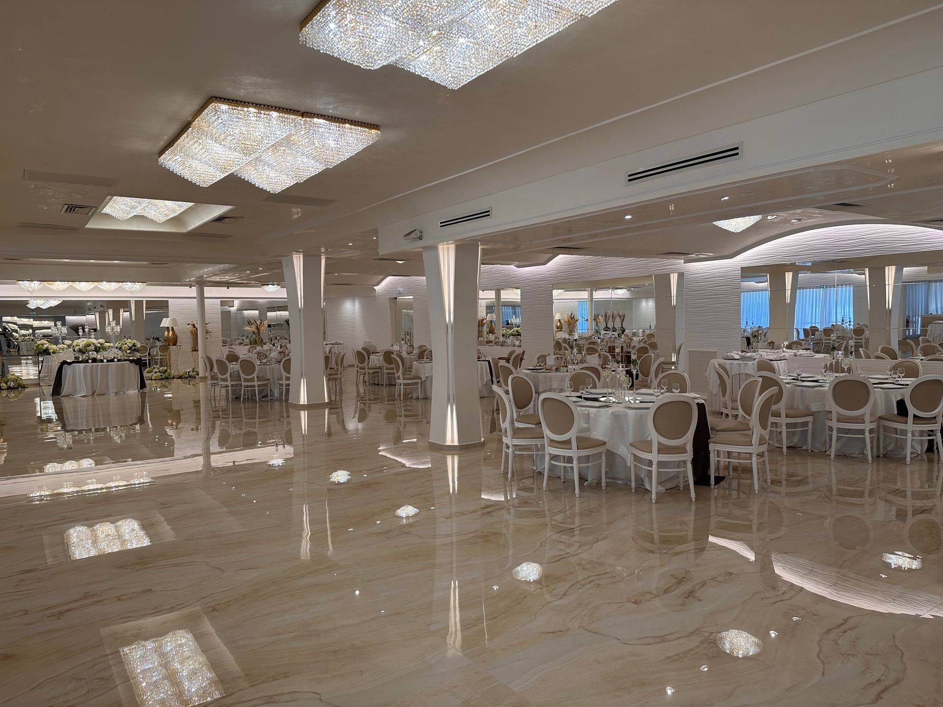 Una grande sala con tavoli e sedie allestita per un ricevimento di nozze.
