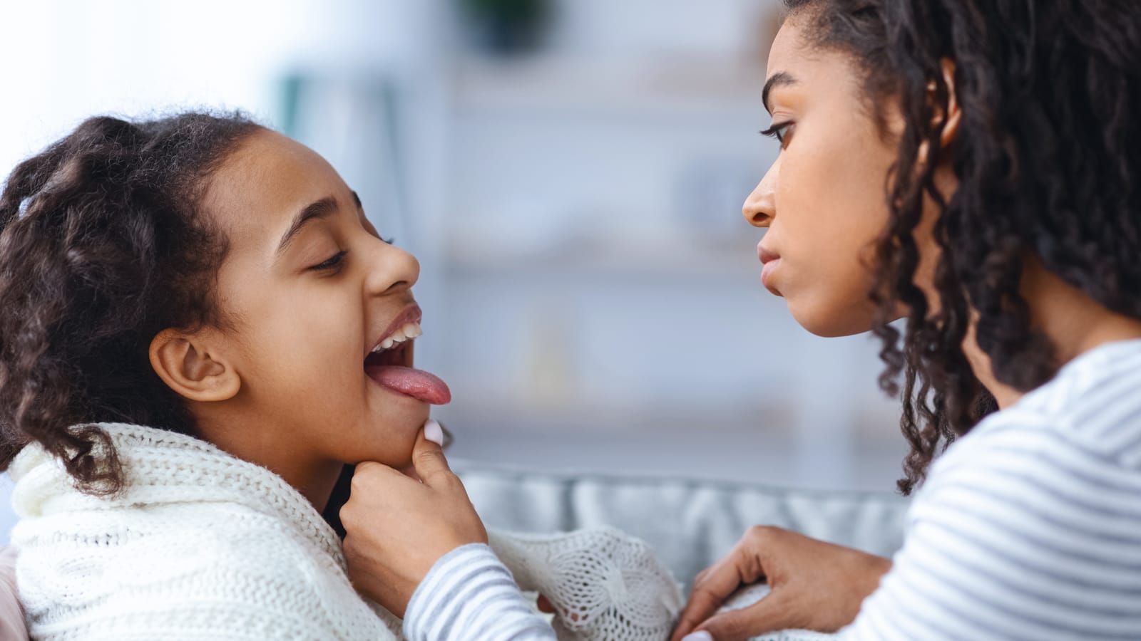 Little girl suffering from tonsillitis, mother checking her throat