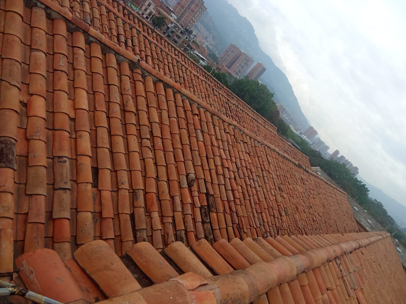 Vista inclinada de un largo tejado de tejas de terracota con edificios distantes y cielo nublado.
