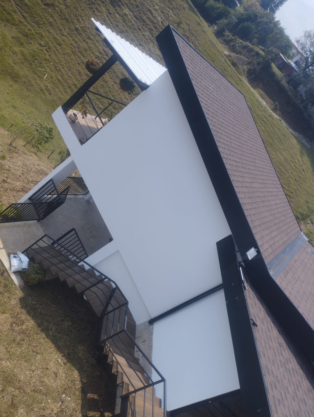 Casa moderna blanca con techo negro y escalera curva en una ladera cubierta de hierba.