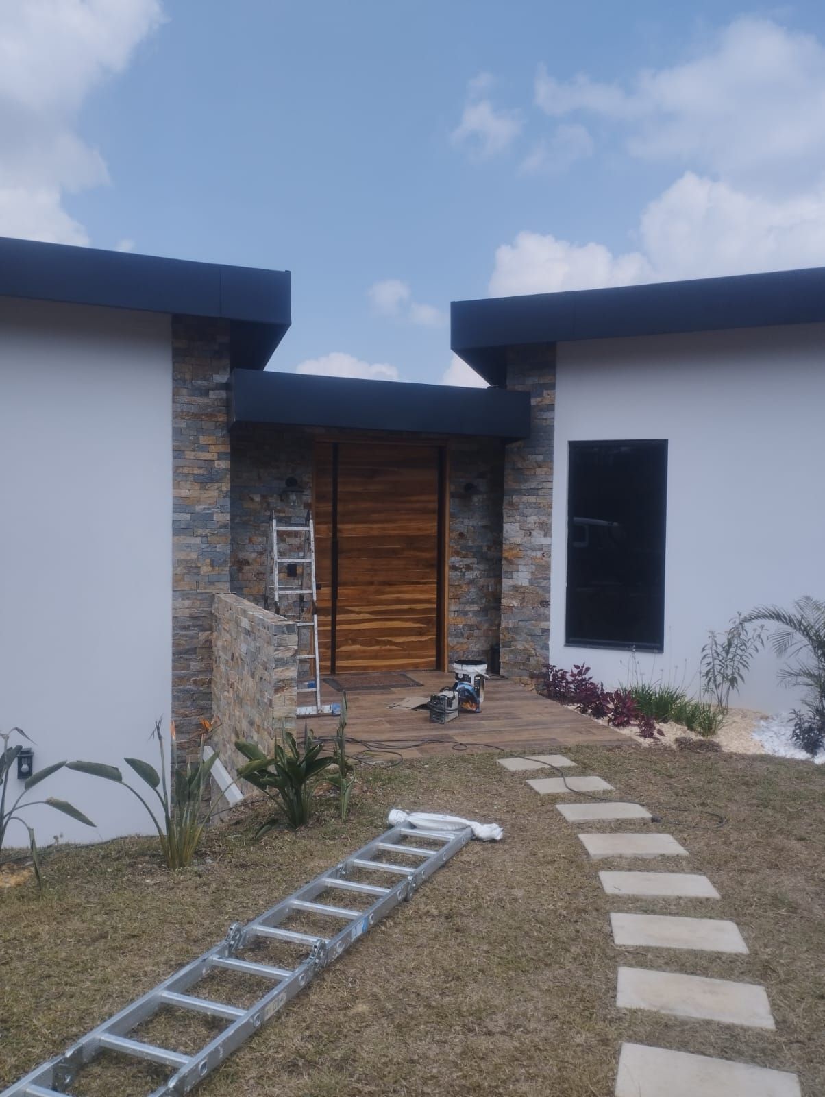 Entrada moderna a la casa con detalles de piedra, puerta de madera, escalones curvos y una escalera en el césped.