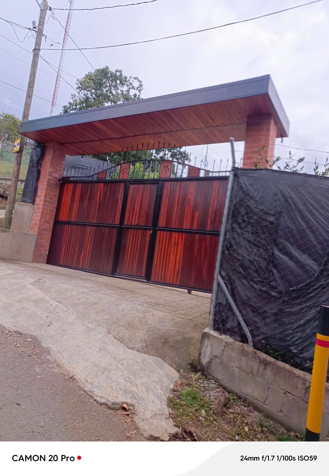 Una puerta y un muro de metal rojo bajo una marquesina de techo azul, junto a una carretera en pendiente.