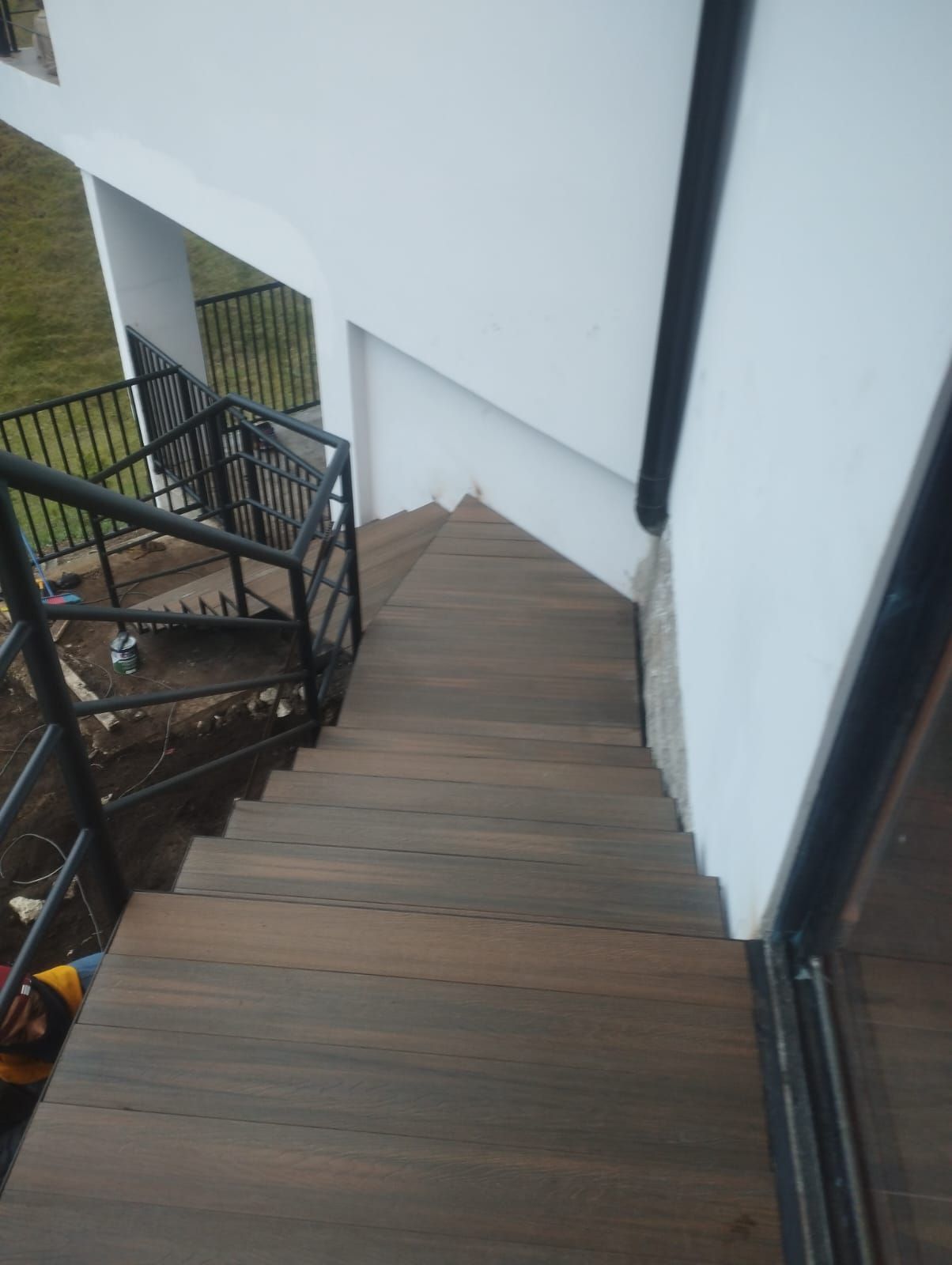 Escalera de madera empinada junto a un edificio blanco con barandilla negra, vista desde lo alto.