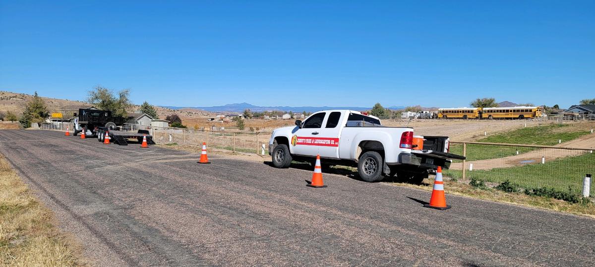 A white truck with orange cones on a gravel road, and a trailer in the background, with a blue sky overhead.