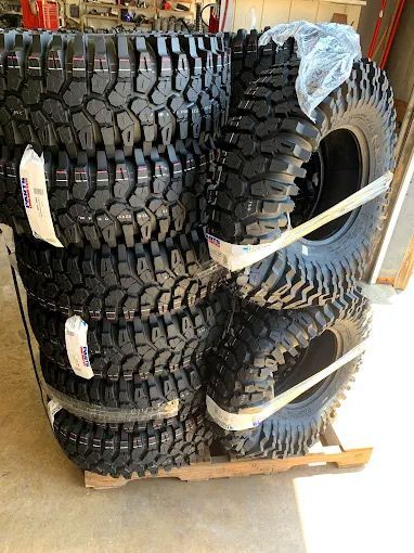 Tires stacked on a wooden pallet, ready for transport. The tires are black with deep treads and secured with white bands.