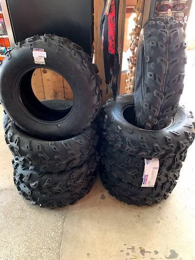 Several new black ATV tires stacked on a wooden floor, with price tags attached.