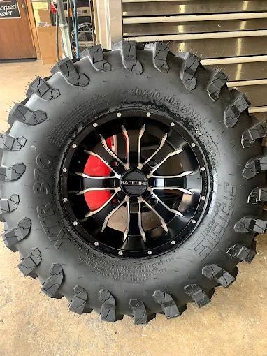 Black and silver ATV wheel with mud tire and red brake caliper.