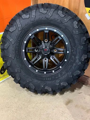 Black off-road tire on a black wheel with silver accents.