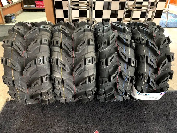 Four black ATV tires lined up, showing large treads on a black mat.