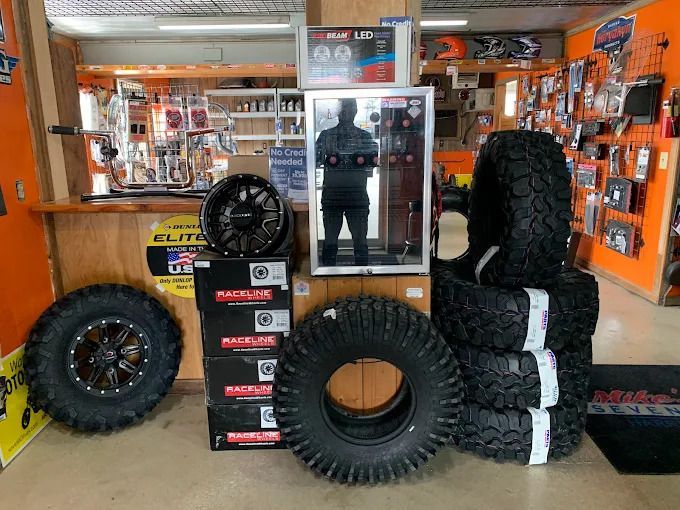 Off-road tire shop display with large black tires, orange walls, and a person reflected in a mirror