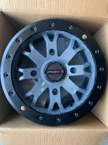 Black and gray alloy wheel with red center cap, packed in a cardboard box