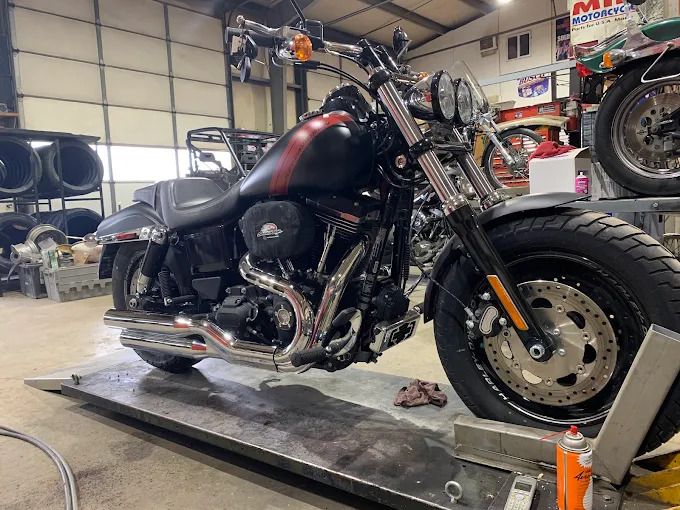 Black motorcycle with chrome details on a shop lift in a garage, shown from the front-left side.