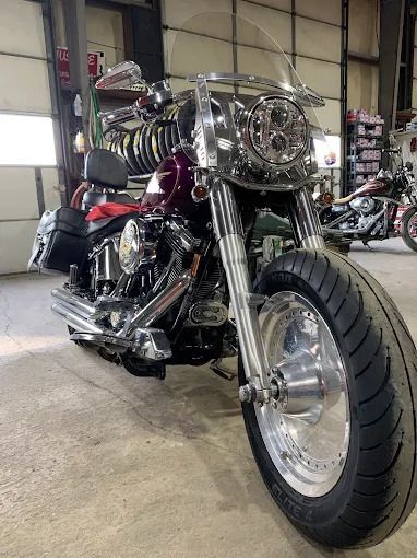 Custom chrome motorcycle with oversized front wheel parked in a garage workshop.