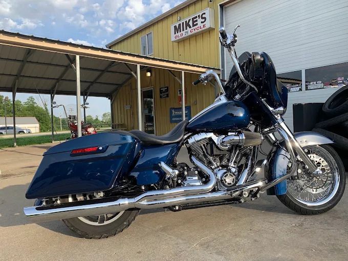Blue touring motorcycle parked outside Mike’s shop under a wooden awning.