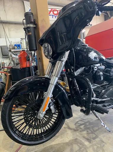 Black touring motorcycle with a large front wheel in a garage or workshop, viewed from the side.