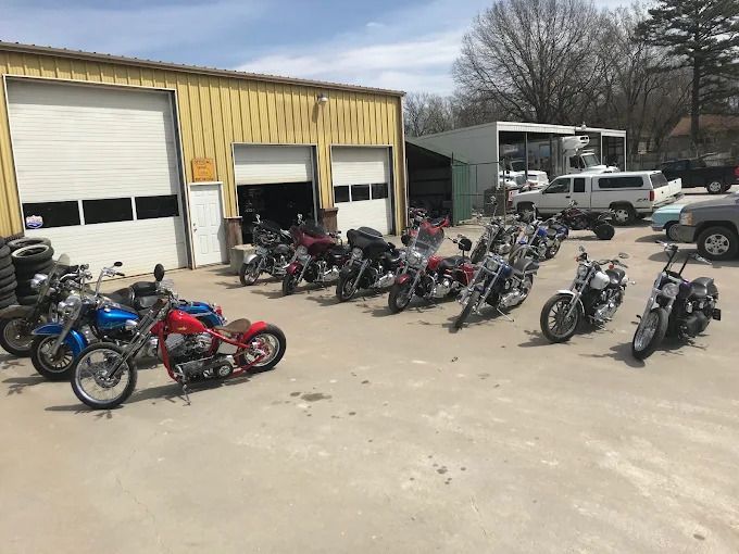 Motorcycles lined up outside a yellow garage with open bays on a sunny day