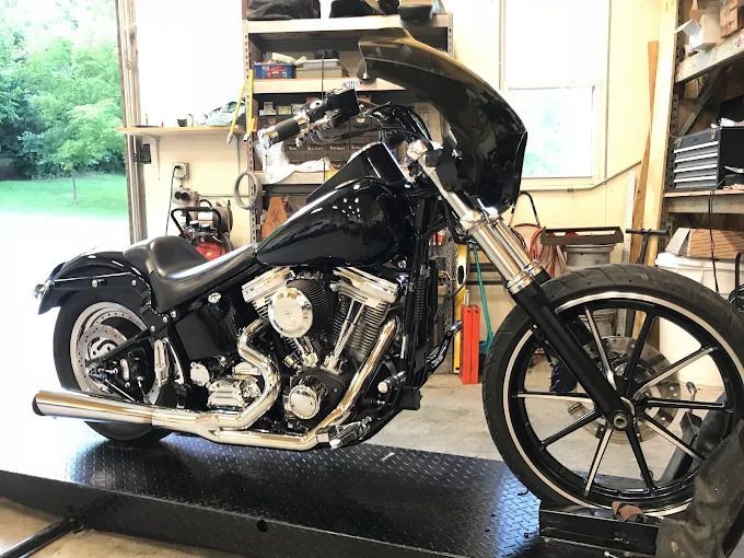 Black custom chopper motorcycle on a lift inside a garage with open doors.