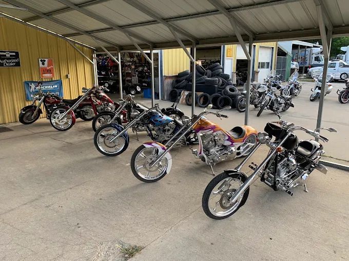 Several custom motorcycles parked under a metal canopy at a motorcycle shop or gathering area