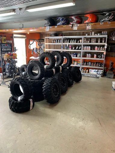 Stacked off-road tires in a garage with shelves of supplies in the background