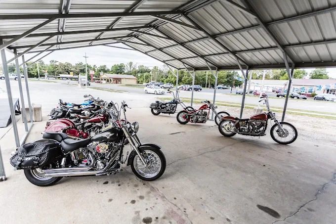 Motorcycles parked under a large open-sided metal canopy in a paved lot