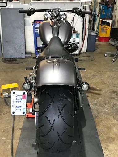 Rear view of a gray motorcycle in a garage, showing a wide rear tire and license plate.