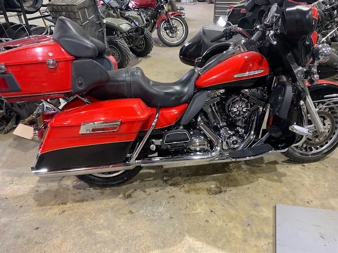 Red touring motorcycle with saddlebags parked indoors on a concrete floor, other bikes in the background