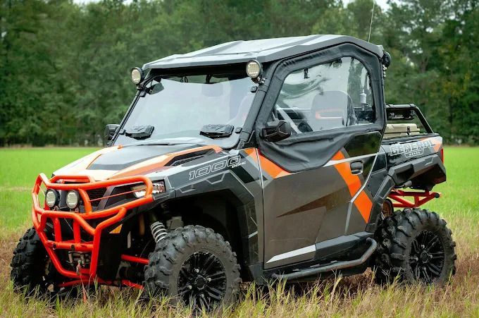 Black and orange off-road UTV with roll cage parked in tall grass, side view