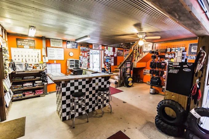 Inside a garage workshop with checkered floor, tools, shelves, and a staircase leading up.