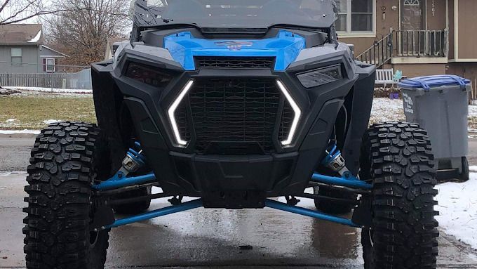 Front view of a blue and black off-road side-by-side vehicle with large tires on a wet driveway