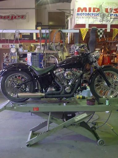 Black motorcycle on a green hydraulic lift in a workshop or showroom
