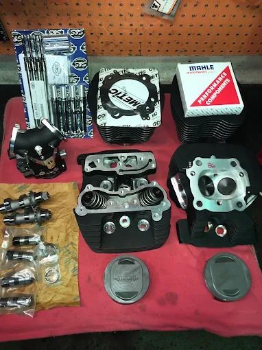 Assorted motorcycle engine parts and gaskets laid out on a red cloth against a pegboard wall.