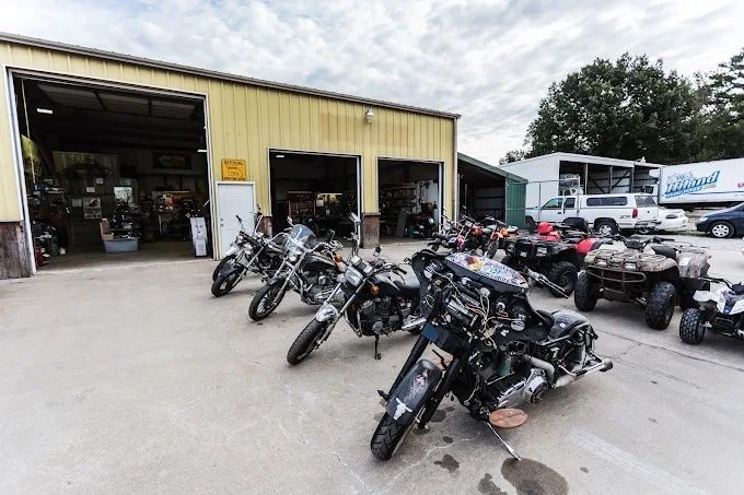 Motorcycles parked outside a yellow garage with open bays and a white RV in the background