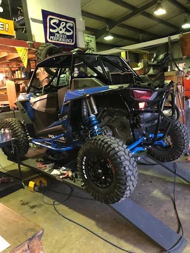 Blue off-road buggy in a garage, raised on a ramp with large knobby tires and exposed suspension.