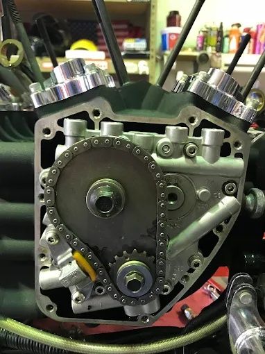 Close-up of a motorcycle engine with exposed timing chain and sprockets on a workbench