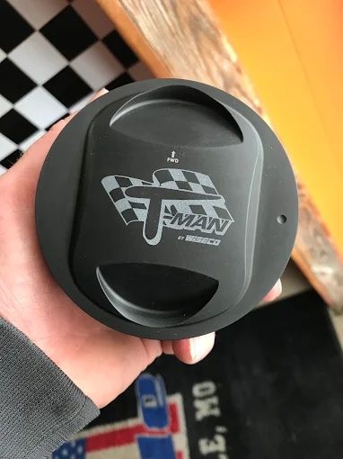 Hand holding a black T-Man racing car part with a checkered flag logo